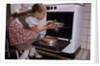 Girl Wearing Apron Removing Cakes from Oven by Anonymous