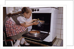 Girl Wearing Apron Removing Cakes from Oven by Anonymous