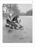 Man Puts Ice Skates On Woman At Rink by Anonymous