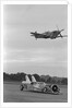 Airplane Flying Over Race Car in Action by Anonymous