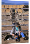 Cowboy and Dog Sitting Against Fence by Anonymous