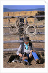 Cowboy and Dog Sitting Against Fence by Anonymous