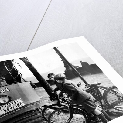 Boys on bicycles cross in front of a tram by Associated Newspapers