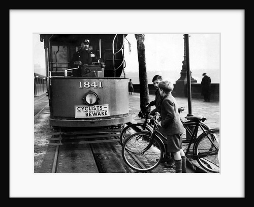 Boys on bicycles cross in front of a tram by Associated Newspapers
