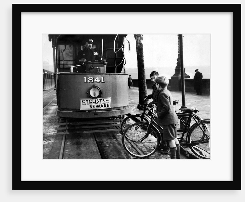 Boys on bicycles cross in front of a tram by Associated Newspapers