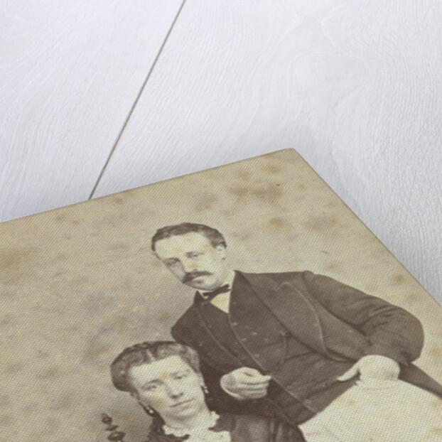 A seated woman with a book in her hands, leaning on her chair, a man in white trousers, one hand in his pocket by F.D. van Rosmalen & Zoon