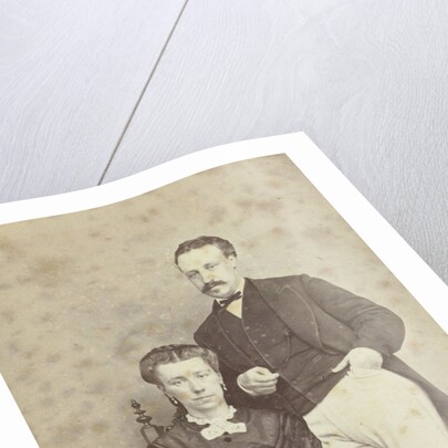 A seated woman with a book in her hands, leaning on her chair, a man in white trousers, one hand in his pocket by F.D. van Rosmalen & Zoon