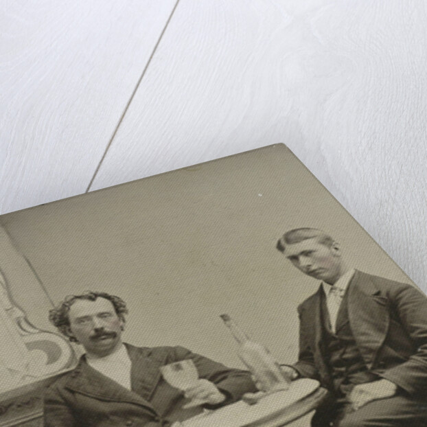 Portrait of two men sitting at the table in a studio, with a bottle and a glass, an imitation salon decor by Anonymous