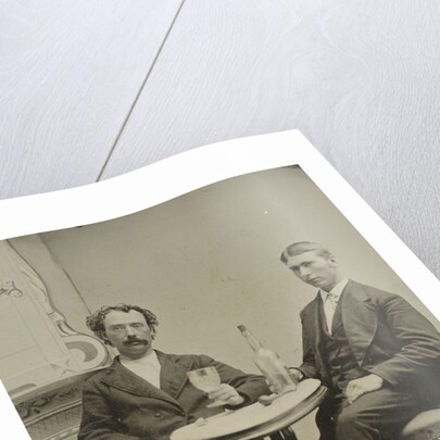 Portrait of two men sitting at the table in a studio, with a bottle and a glass, an imitation salon decor by Anonymous