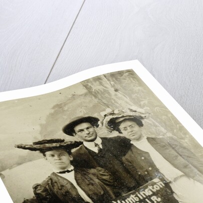 Portrait of a man and two women in front of a painted backdrop (tree, lake and mountains) and a sign that read 'Huntington FAIR 1905 by Anonymous