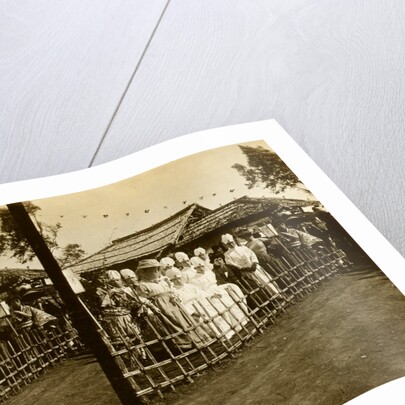 Group portrait of Japanese medical personnel and others dressed in Western and traditional style clothing seated near a building over which hang small flags by Anonymous