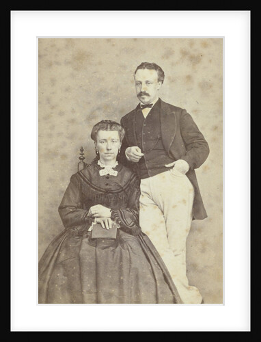 A seated woman with a book in her hands, leaning on her chair, a man in white trousers, one hand in his pocket by F.D. van Rosmalen & Zoon