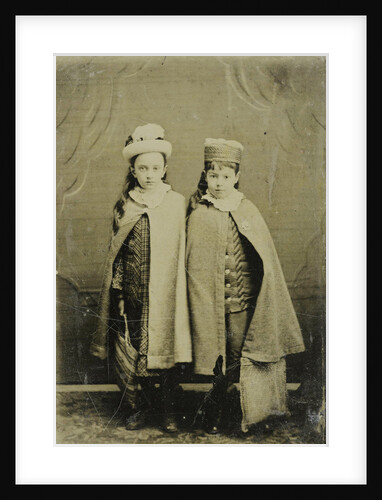 Portrait of two girls with hats and capes, standing in a studio setting by Anonymous
