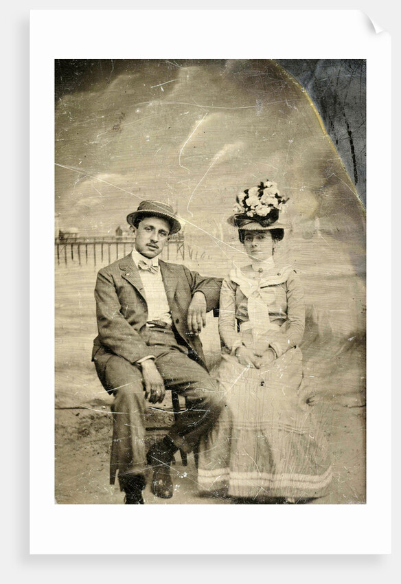 Portrait of a man and woman sitting in front of a painted backdrop (beach, sea and pier) by Anonymous