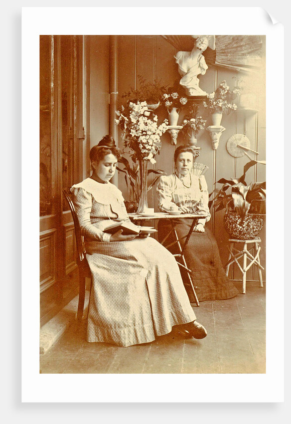 Two women sitting in a greenhouse, one reading by Anonymous