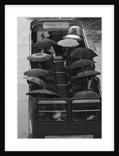 Tourists sit underneath their umbrellas on the top deck of an open top bus by Kent Gavin