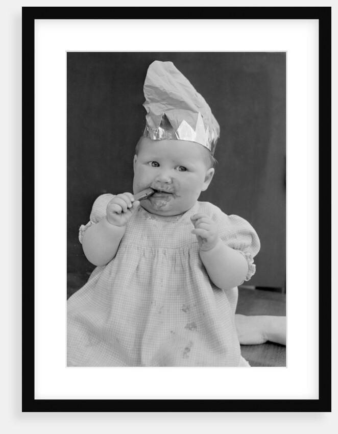 Baby wearing a party hat and eating a Cadbury chocolate finger by Staff