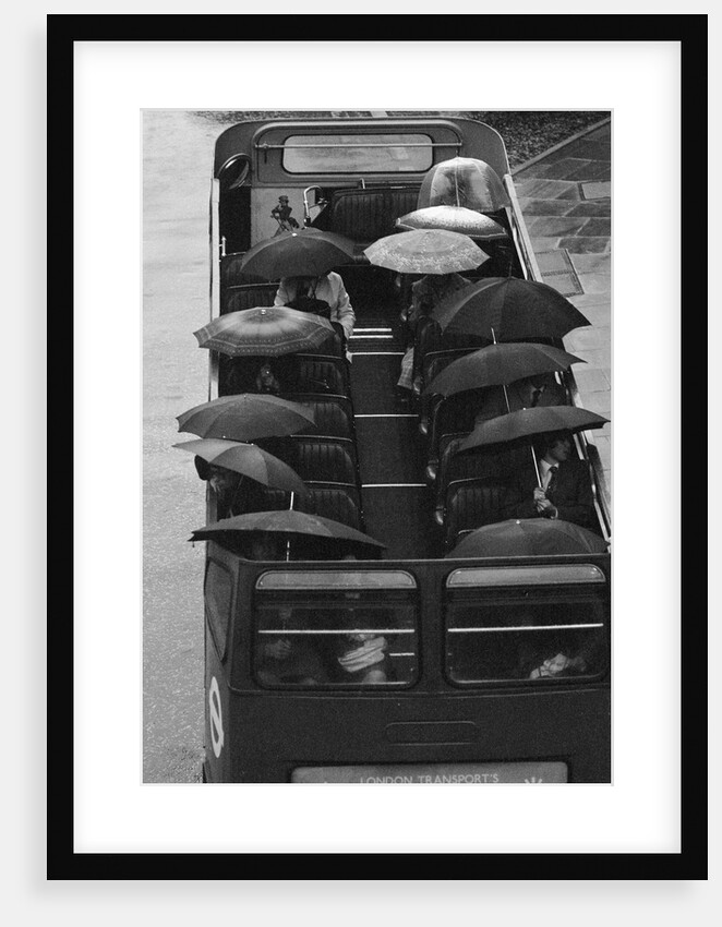 Tourists sit underneath their umbrellas on the top deck of an open top bus by Kent Gavin