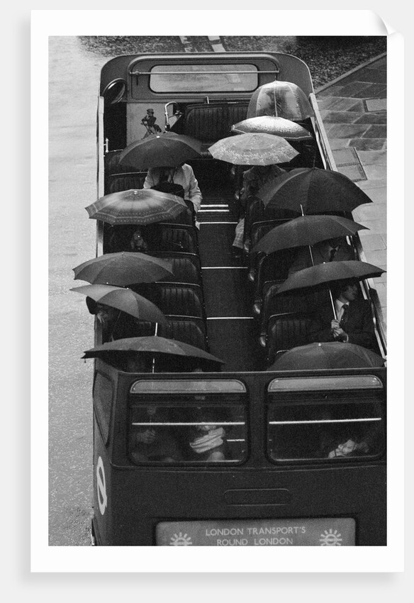 Tourists sit underneath their umbrellas on the top deck of an open top bus by Kent Gavin