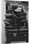 Tourists sit underneath their umbrellas on the top deck of an open top bus by Kent Gavin