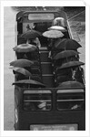 Tourists sit underneath their umbrellas on the top deck of an open top bus by Kent Gavin