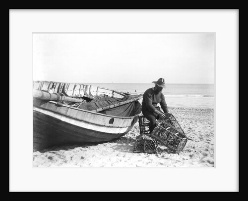 A fisherman in sou'wester mending lobster/crab creels on the beach alongside a beached Sheringham crab boat by Smiths Suitall Ltd.