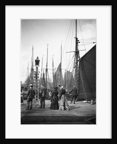 Men and women onlookers at the end of the quay looking at the forest of masts and sails in the harbour at Lowestoft, Suffolk by Smiths Suitall Ltd.