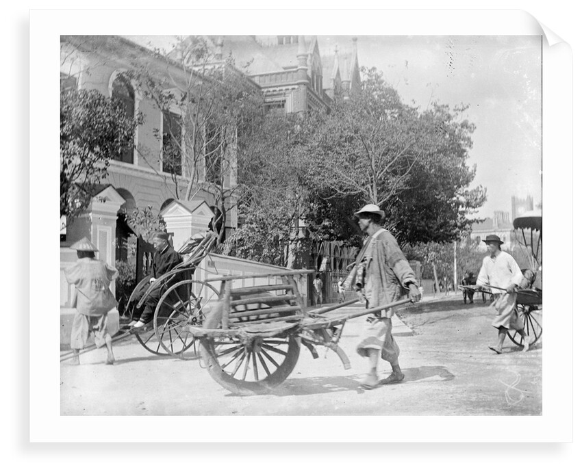 A Chinese man pushing a wooden wheelbarrow with a rickshaw in the background by Kenneth Hurlstone Jones