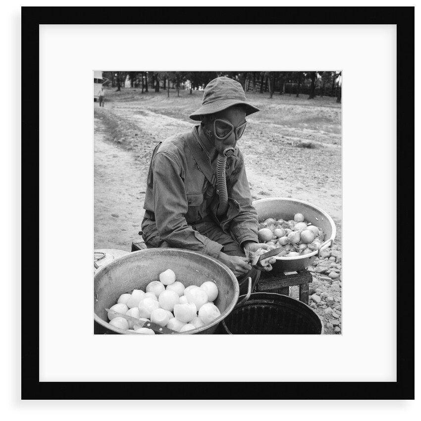 American soldier peeling onions while wearing a gas mask by Alan Villiers