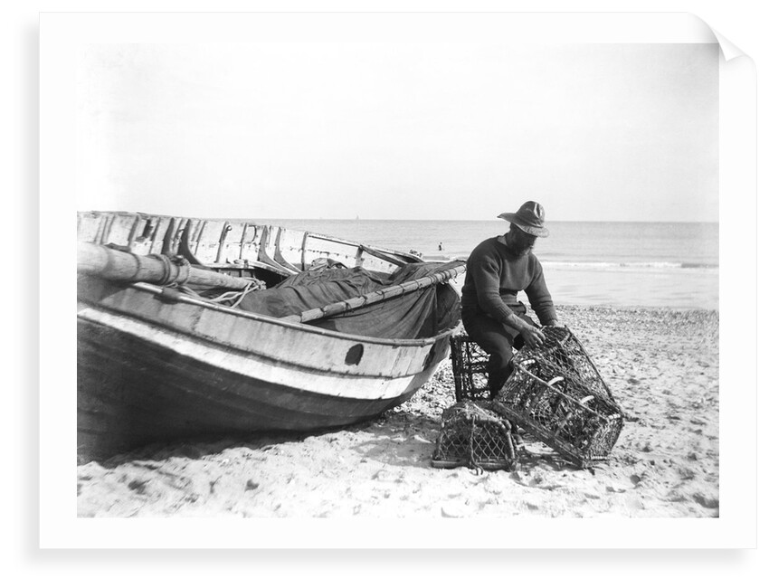A fisherman in sou'wester mending lobster/crab creels on the beach alongside a beached Sheringham crab boat by Smiths Suitall Ltd.