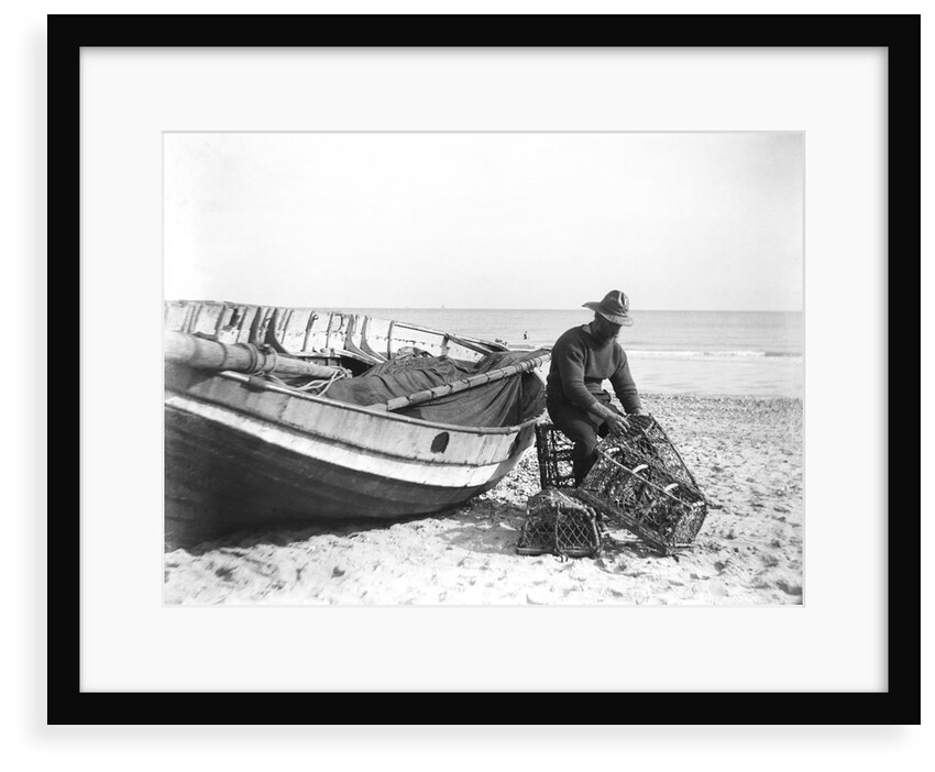 A fisherman in sou'wester mending lobster/crab creels on the beach alongside a beached Sheringham crab boat by Smiths Suitall Ltd.