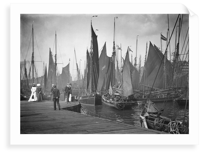 A view from the wooden quay at Lowestoft, Suffolk, looking across the trawl basin filled with a large number of sailing trawlers by Smiths Suitall Ltd.