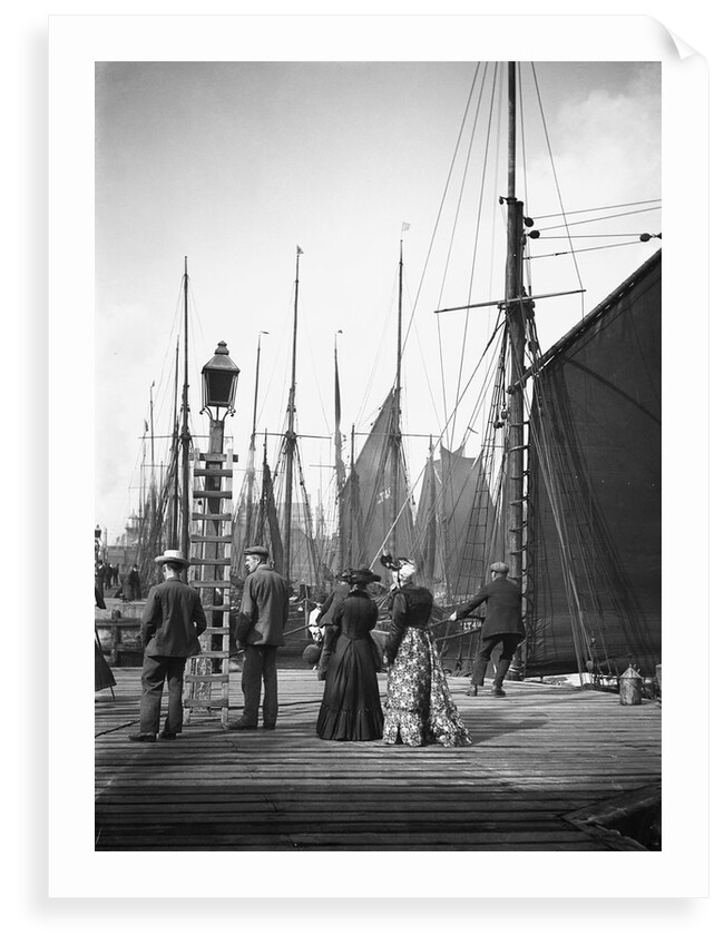 Men and women onlookers at the end of the quay looking at the forest of masts and sails in the harbour at Lowestoft, Suffolk by Smiths Suitall Ltd.