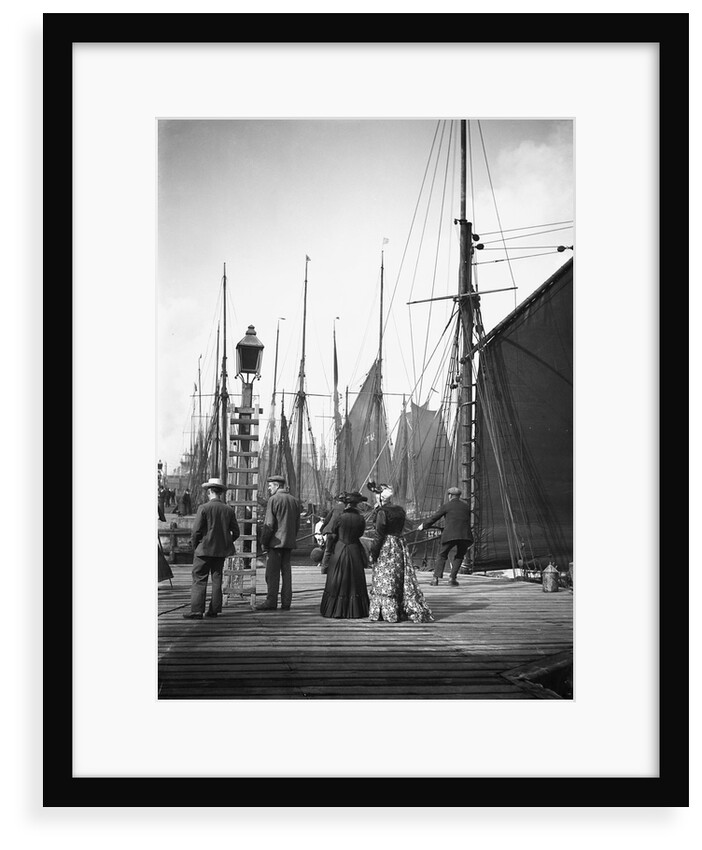 Men and women onlookers at the end of the quay looking at the forest of masts and sails in the harbour at Lowestoft, Suffolk by Smiths Suitall Ltd.