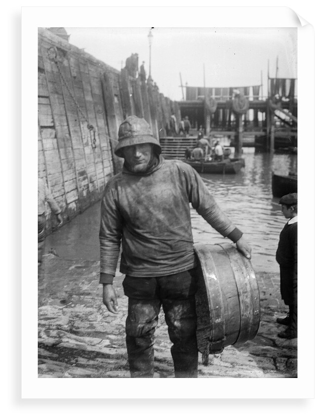 A Folkestone fisherman in smock and sou'wester carrying a tub for fish on the slipway by unknown