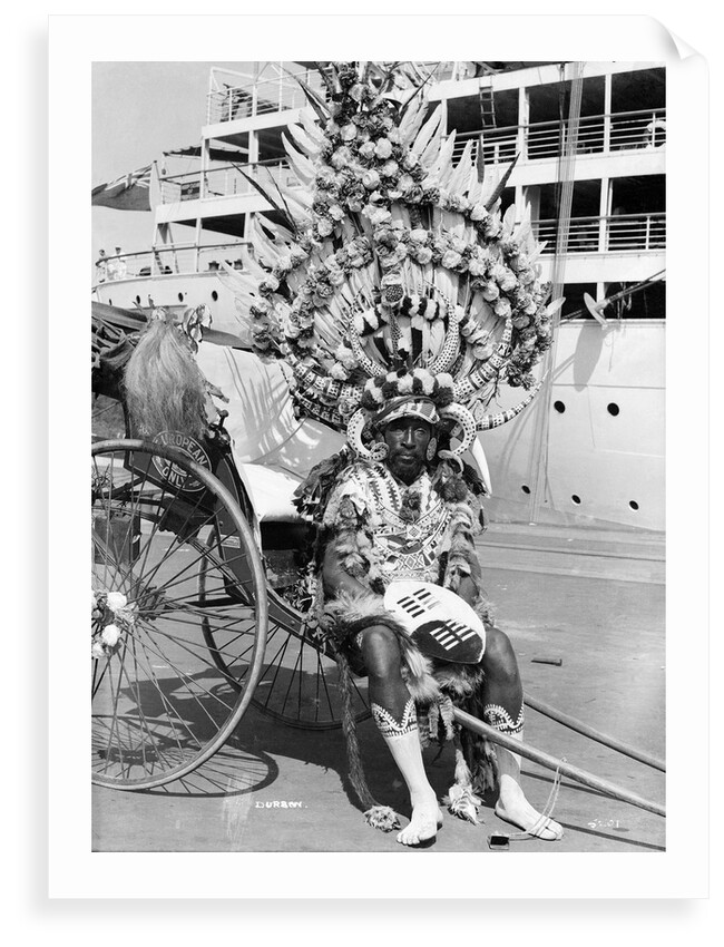 A local rickshaw driver in 'traditional' costume, with a Union-Castle Line ship in the background, at Durban, South Africa by Marine Photo Service
