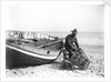 A fisherman in sou'wester mending lobster/crab creels on the beach alongside a beached Sheringham crab boat by Smiths Suitall Ltd.