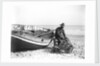 A fisherman in sou'wester mending lobster/crab creels on the beach alongside a beached Sheringham crab boat by Smiths Suitall Ltd.