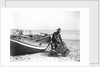 A fisherman in sou'wester mending lobster/crab creels on the beach alongside a beached Sheringham crab boat by Smiths Suitall Ltd.