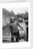 A Folkestone fisherman in smock and sou'wester carrying a tub for fish on the slipway by unknown