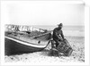 A fisherman in sou'wester mending lobster/crab creels on the beach alongside a beached Sheringham crab boat by Smiths Suitall Ltd.