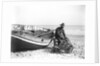 A fisherman in sou'wester mending lobster/crab creels on the beach alongside a beached Sheringham crab boat by Smiths Suitall Ltd.