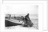 A fisherman in sou'wester mending lobster/crab creels on the beach alongside a beached Sheringham crab boat by Smiths Suitall Ltd.