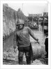 A Folkestone fisherman in smock and sou'wester carrying a tub for fish on the slipway by unknown