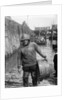 A Folkestone fisherman in smock and sou'wester carrying a tub for fish on the slipway by unknown