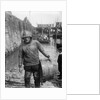 A Folkestone fisherman in smock and sou'wester carrying a tub for fish on the slipway by unknown