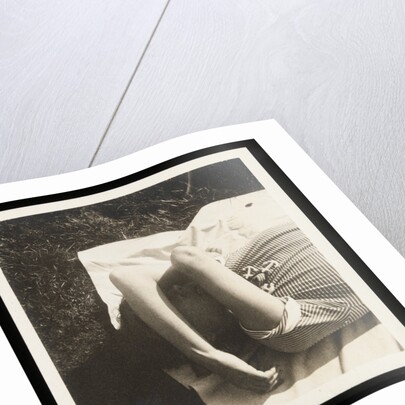 Woman wearing striped t-shirt lying on rug with both arms covering face by Curtis Moffat