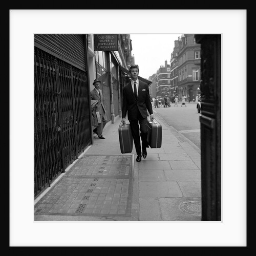 Mark Wynter, English actor and singer, walking down street with suitcases by Harry Hammond